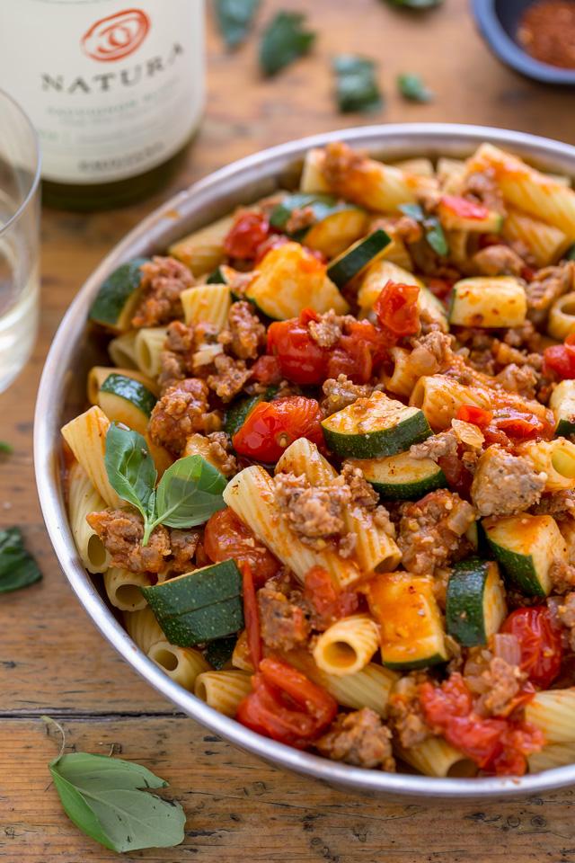 Pan of rigatoni pasta on a table with white wine and fresh basil