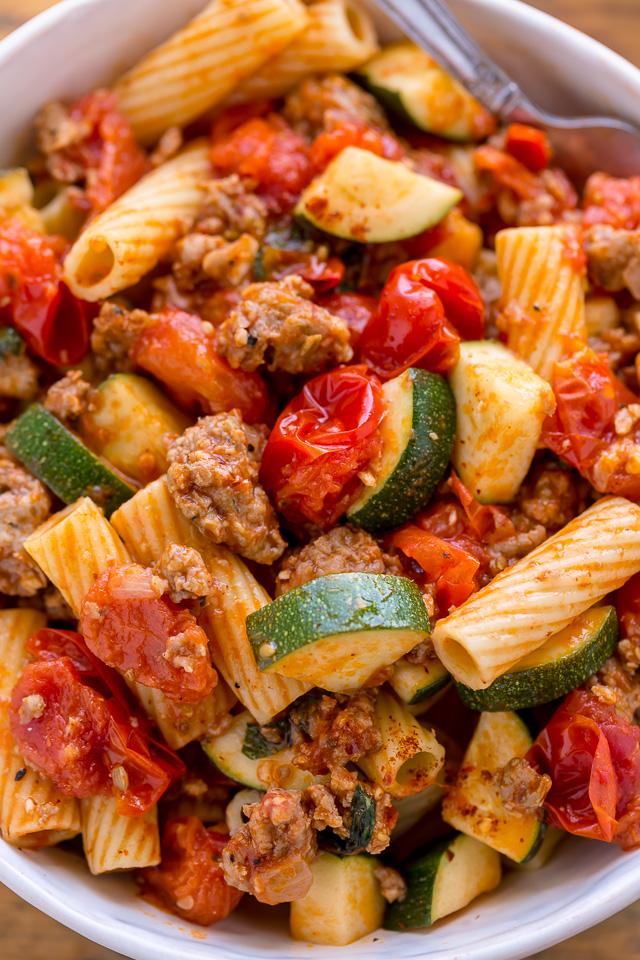 Rigatoni with sausage, zucchini, and tomato sauce in a white bowl.