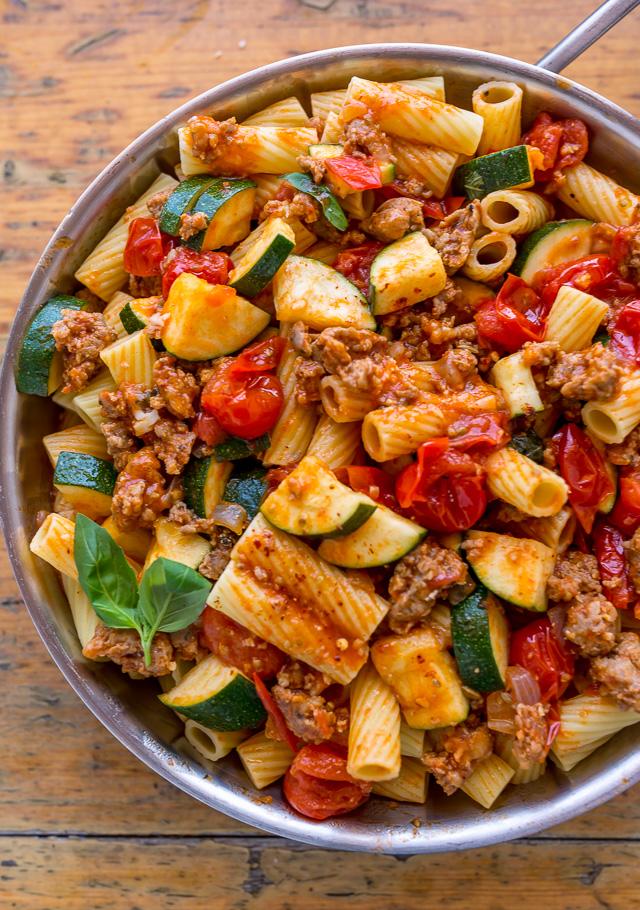 Sausage rigatoni with zucchini and tomato sauce in a stainless steel skillet.