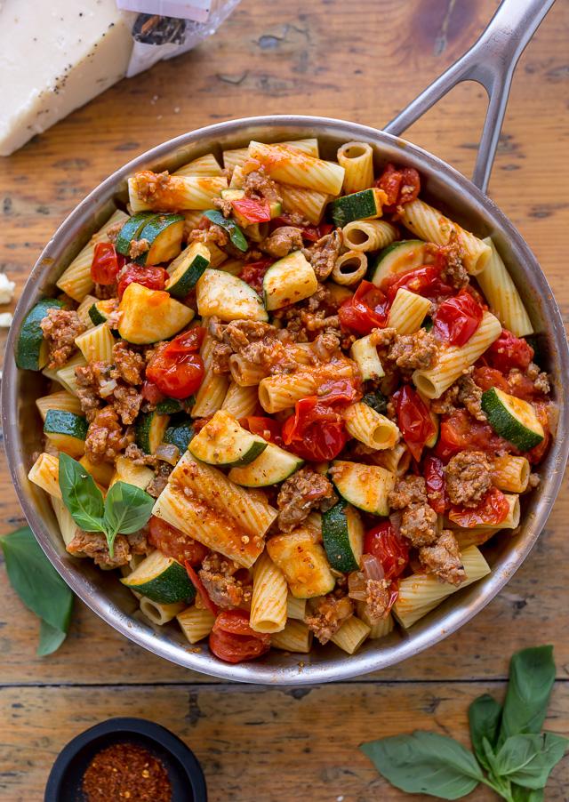 Skillet with rigatoni pasta on a wooden table.