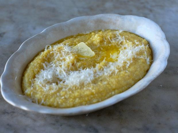 creamy polenta in a white serving bowl topped with butter and grated cheese