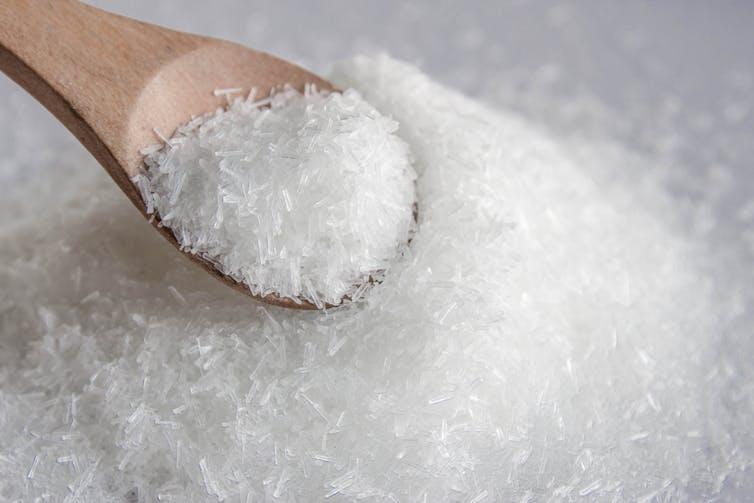 a pile of white, long crystals scooped with a small wooden spoon.