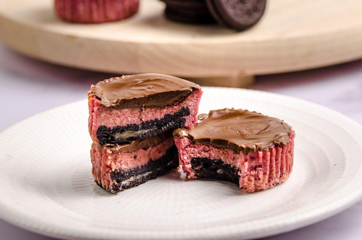 3 mini red velvet oreo cheesecakes on a plate, one with a bite missing