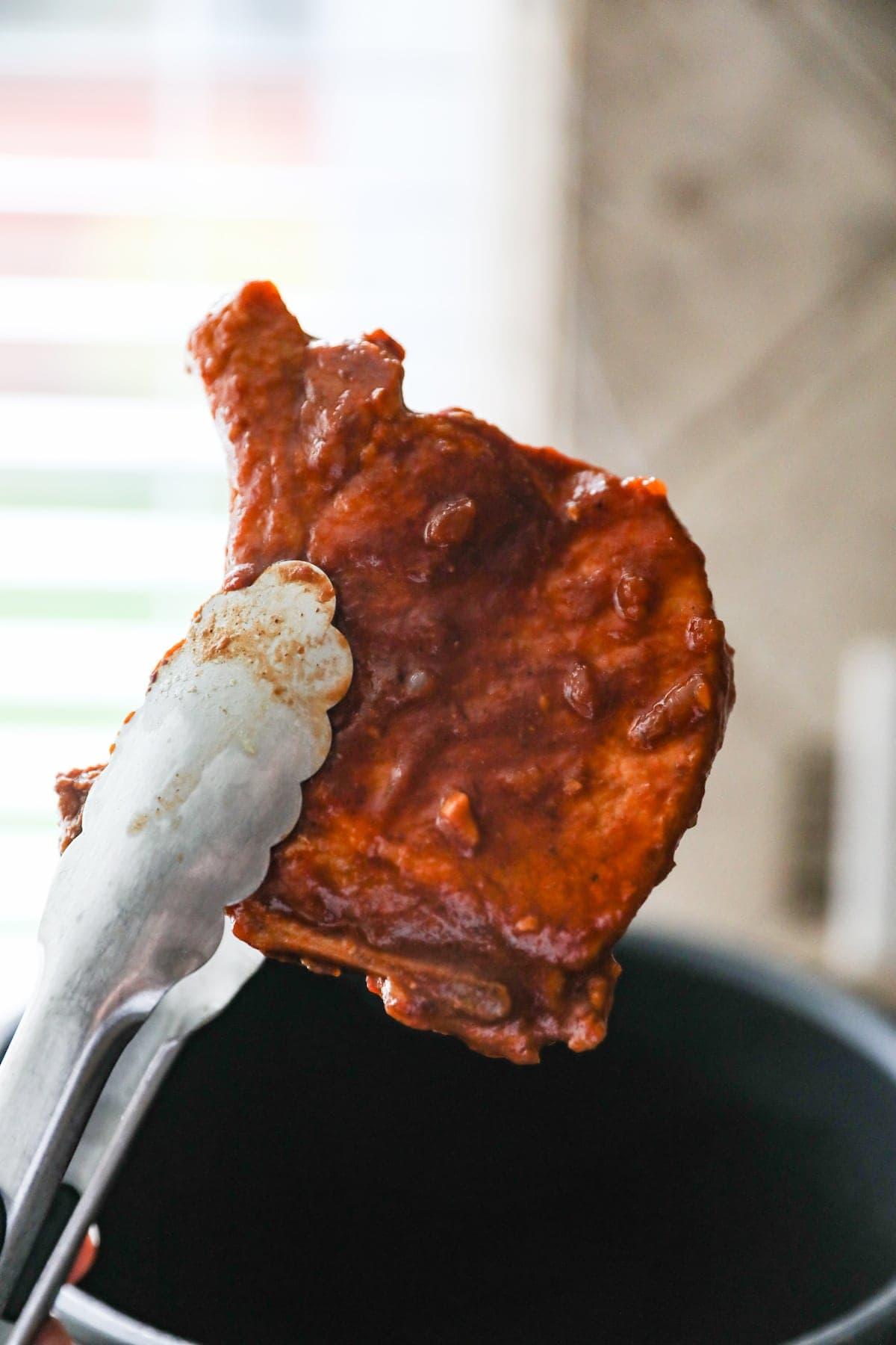 tongs holding cooked pork chop with sauce
