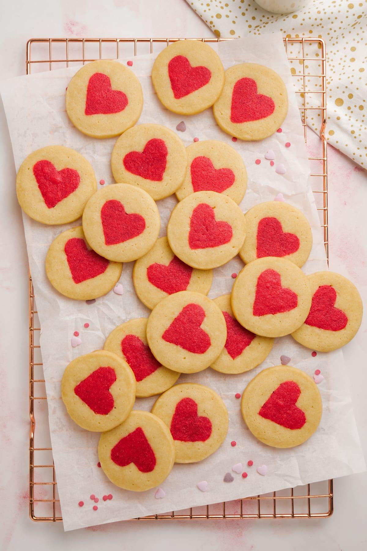 valentines day cookies 19 white cookies with red hearts in the middle spread out on parchment paper and cooling rack