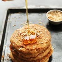 Pouring maple syrup onto a stack of delicious Vegan Toasted Coconut Pancakes