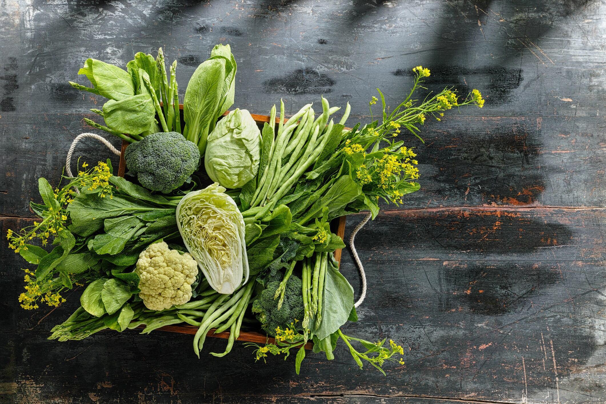 Market fresh green leaf vegetables in an old wooden crate on an old wooden table. Vegetables include, broccoli, cauliflower, cabbage, spring greens, bok choy, spinach and choy sum.