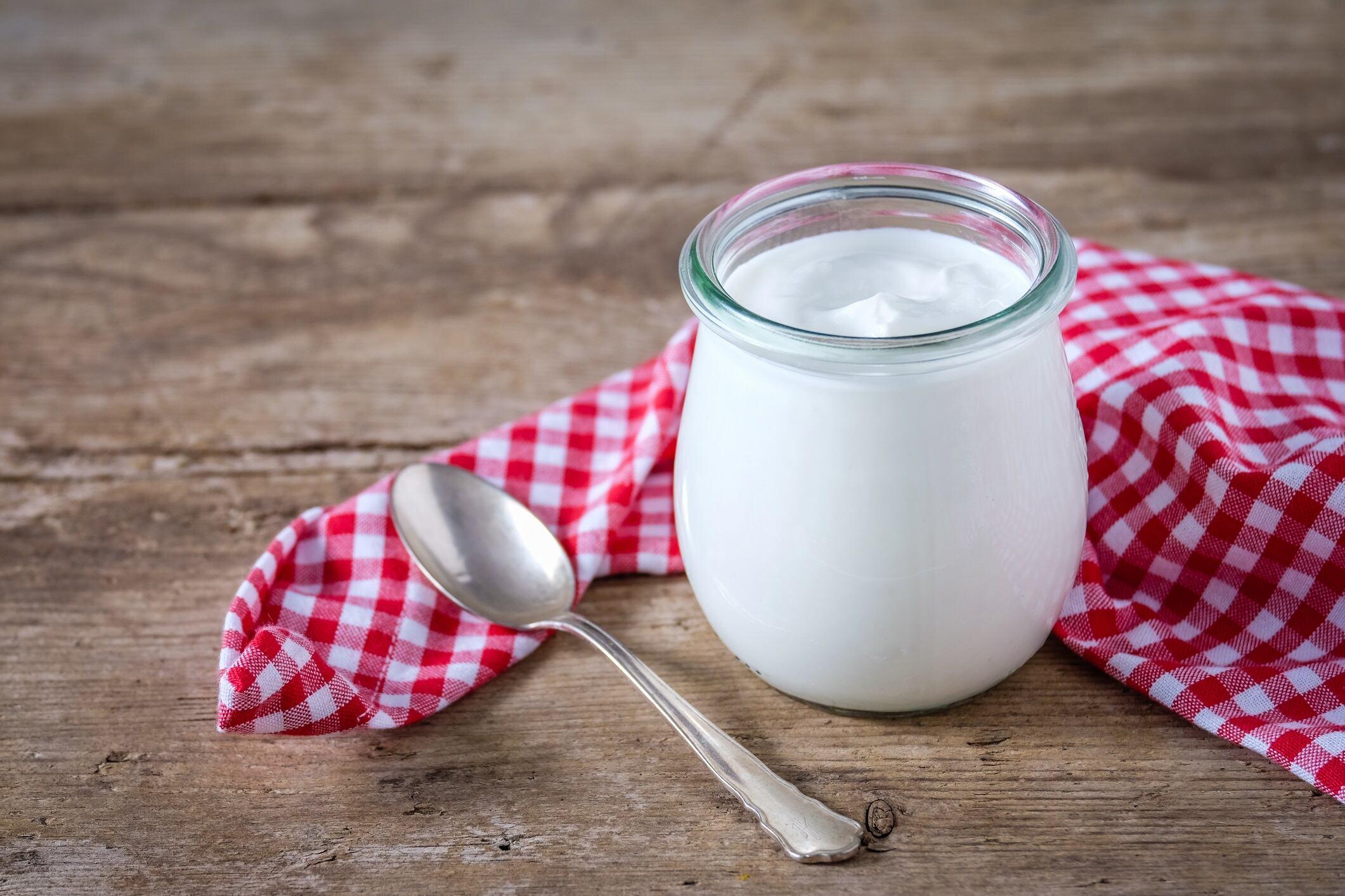 Fresh natural yoghurt in a preserving jar on a wooden table.