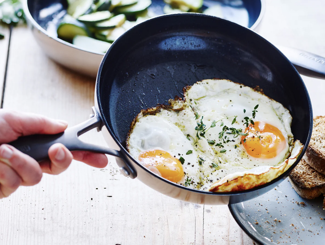 Image of the GreenPan Venice Pro Noir ceramic nonstick fry pan, getting ready to release two sunny-side up eggs onto a plate.